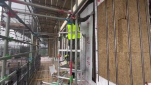 A site operative on a construction site applying protective board to a window for temporary surface protection
