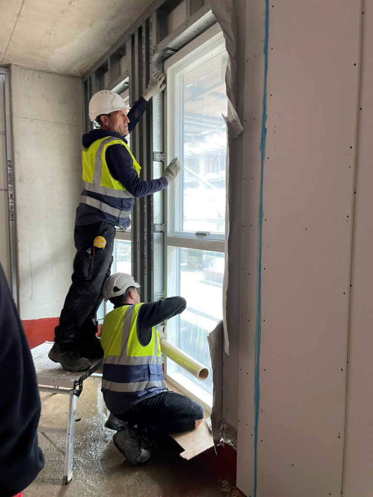 two construction workers applying a roll of protective film to a window