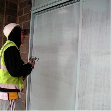 a cpnstruction worker using an airless spray gun to apply Protectapeel to a large pane of glass and the frames on a construction site