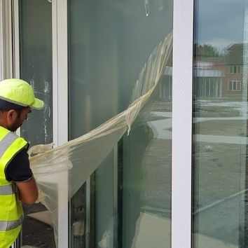 A construction worker peeling Protectapeel protective coating from a large pane of glass on a construction site