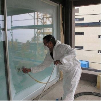 a man in white overalls spraying Protectapeel protective coating to a large glass panel on a construction site