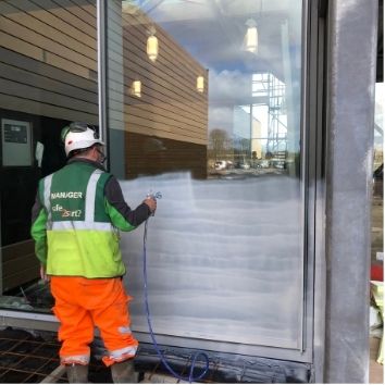 construction worker using an airless spray gun to apply Protectapeel to a glass façade on a construction site