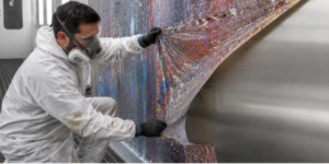 Peeling Protectapeel Boothstrip from a spraybooth wall, the coating is covered in paint overspray but when peeled back the spray booth wall is clean and undamaged